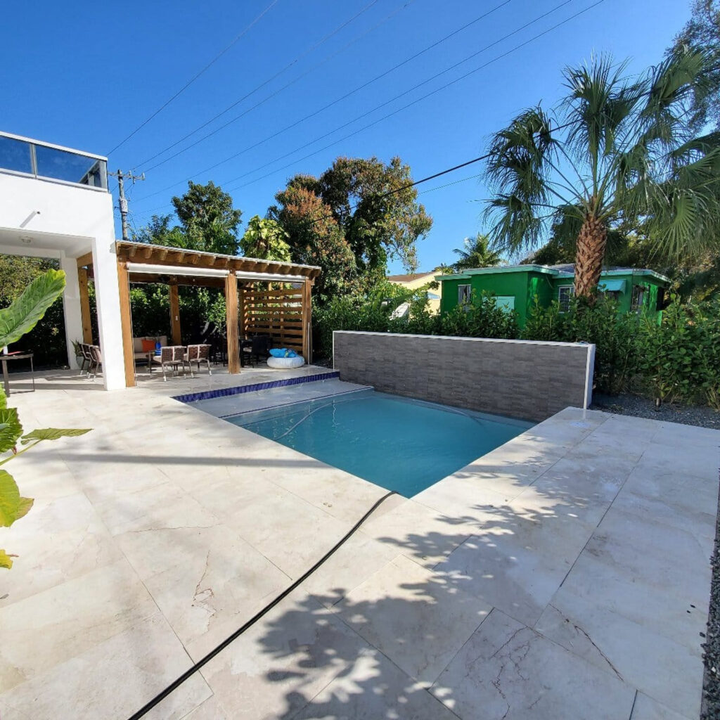 A small modern plunge pool with a stone accent wall on a paved patio beside a wooden pergola.
