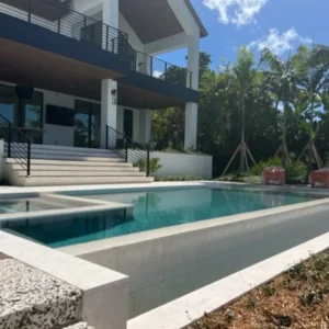 A modern two-tier rectangular pool with turquoise water beside a contemporary two-story home surrounded by palm trees.