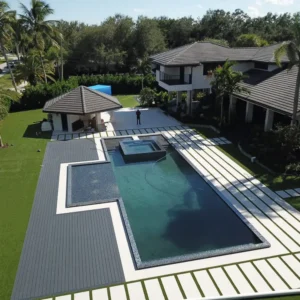 Aerial view of a large modern rectangular pool with an attached raised spa and tanning ledge beside a luxury home.