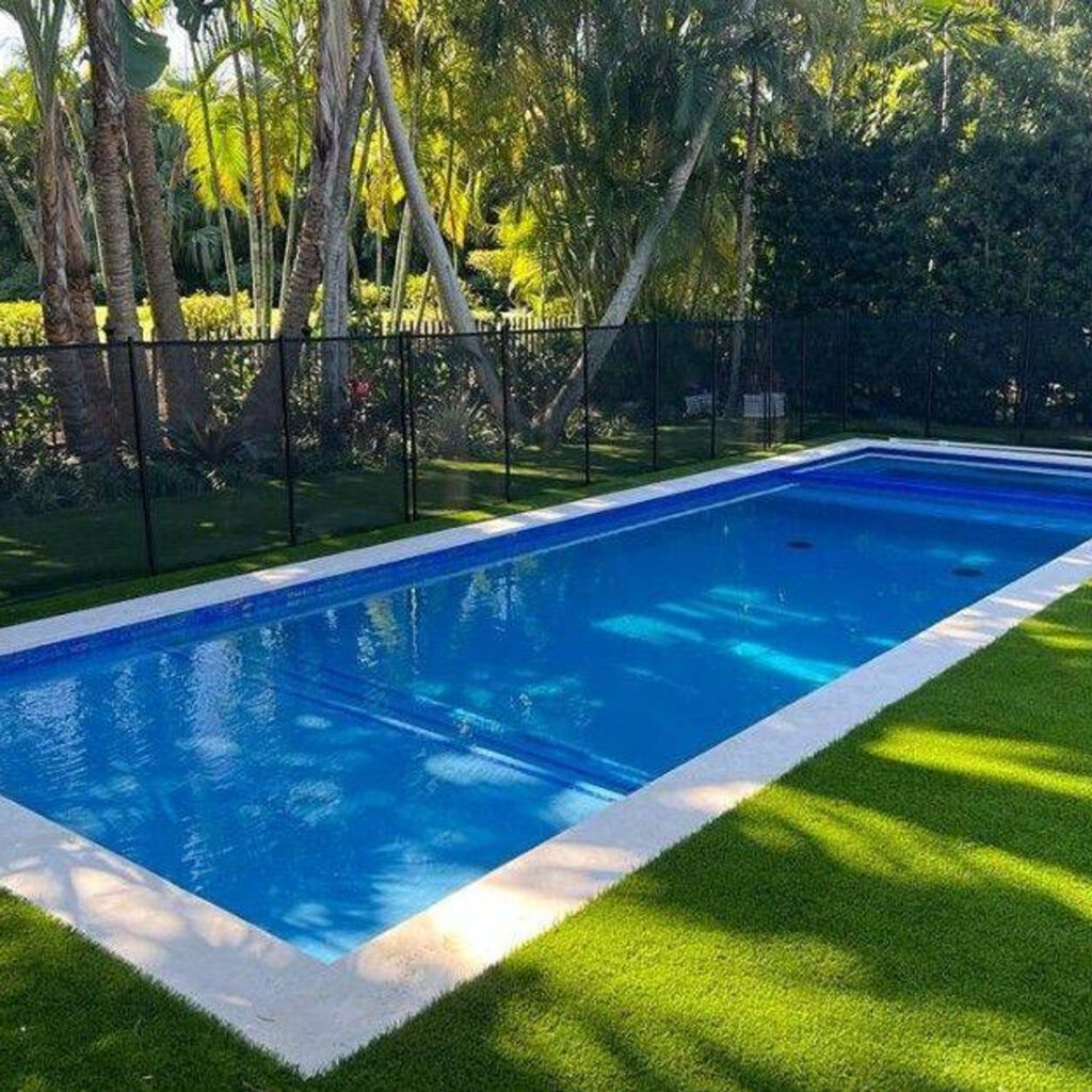 A rectangular vinyl-liner pool surrounded by artificial turf and palm trees with a black safety fence.