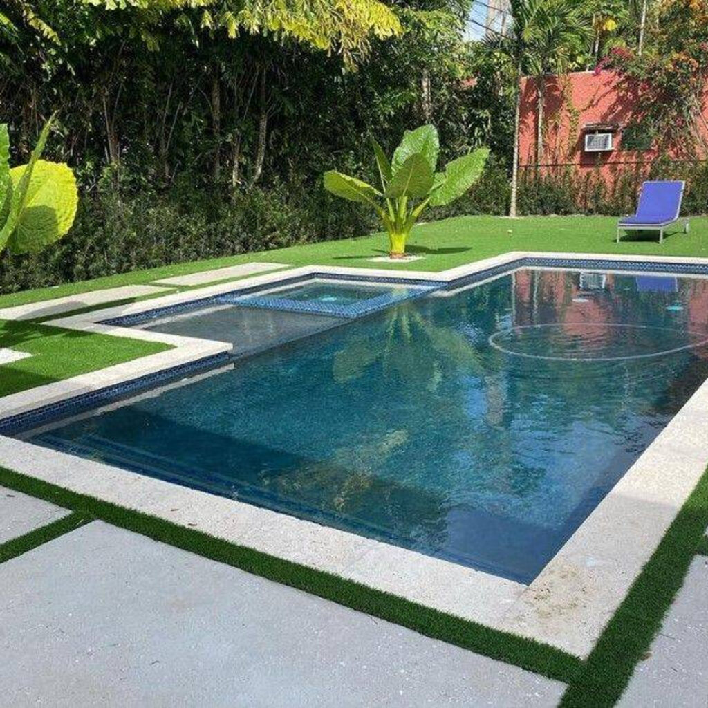 A rectangular backyard pool with an attached spa at one end, surrounded by turf and concrete pavers.