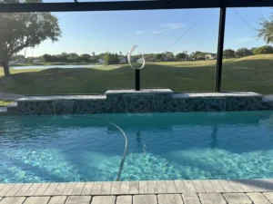 A screened pool with a raised tiled wall and three scupper waterfalls overlooking a golf course and pond.