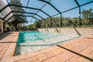 Screened rectangular pool with a stacked-stone raised wall and deck jets spraying arcs into the water.