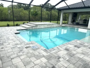 A rectangular pool under a screen enclosure with a raised stone sun platform and steps beside an outdoor kitchen and fireplace.