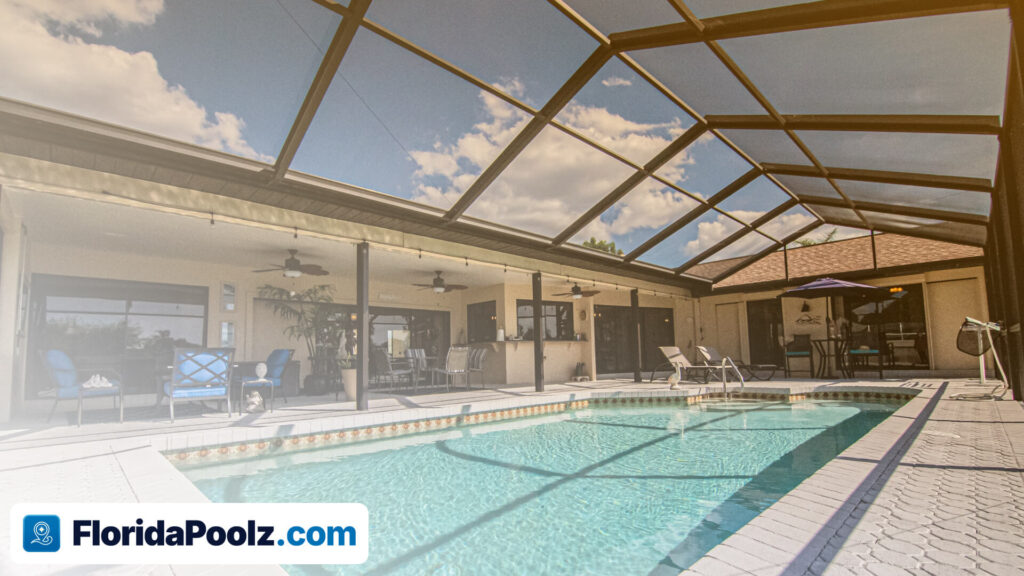 The inside of a screened pool enclosure, its aluminium frame and mesh roof over a pool and patio seating.