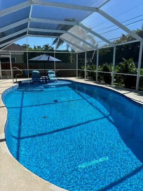 A freeform vinyl-lined pool under a screened lanai with patio chairs and umbrella.