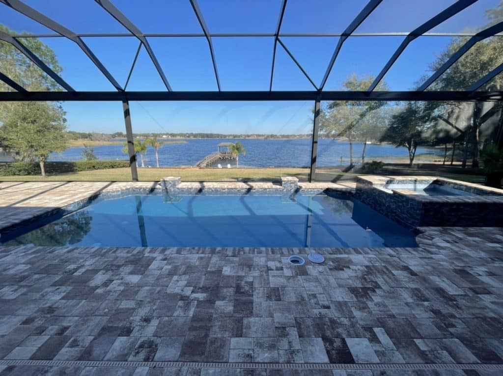 Screened rectangular pool with raised spa and water bowls overlooking a lake with a dock.