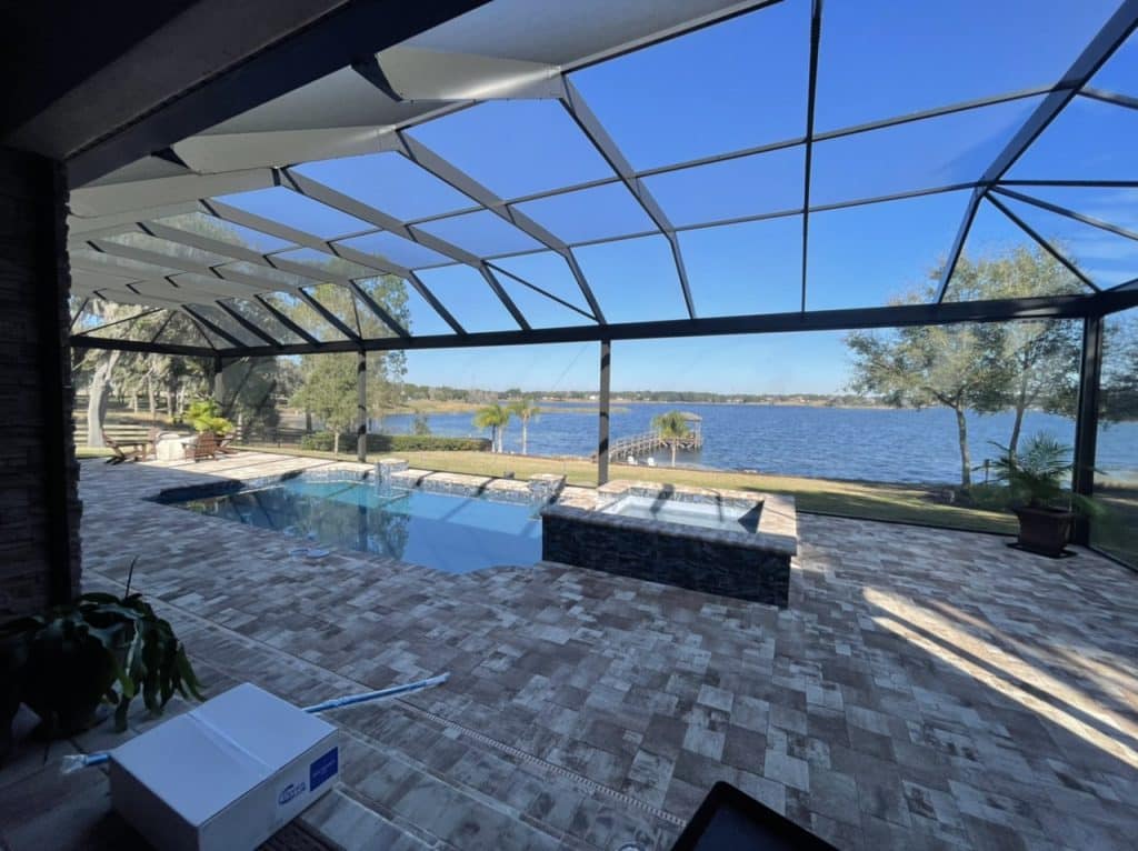 Rectangular lakefront pool with a raised stone spa under a large screened lanai overlooking open water.