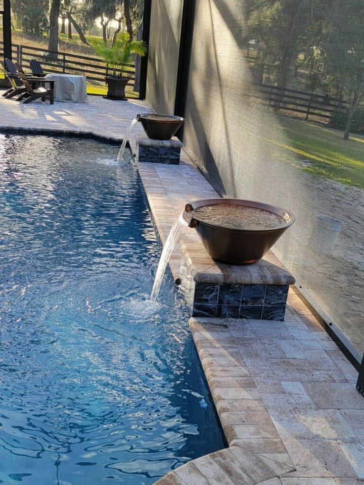 Two copper water bowls spill into a pool edge under a screened lanai.