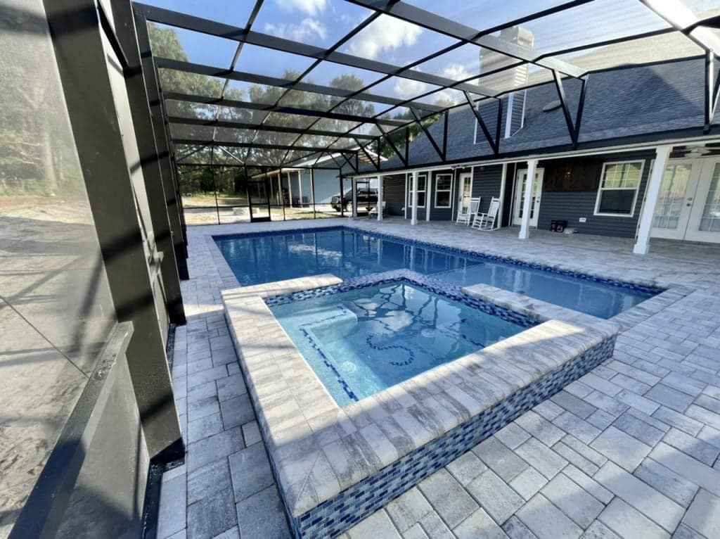 A rectangular pool with a raised spa featuring blue mosaic tile, under a screened patio enclosure.