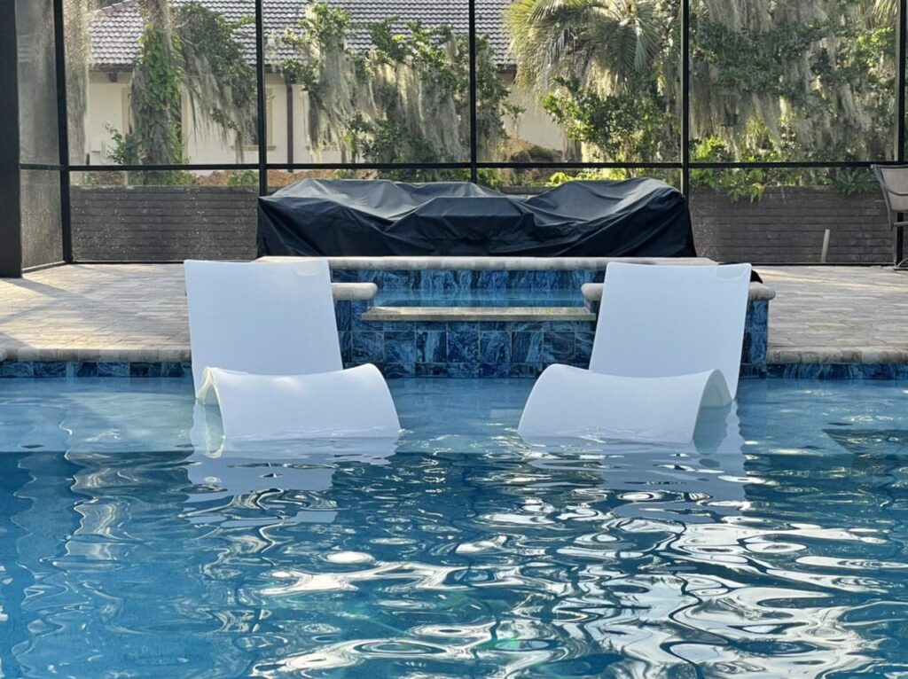 Two in-pool loungers submerged near a tiled raised wall inside a screened pool enclosure.