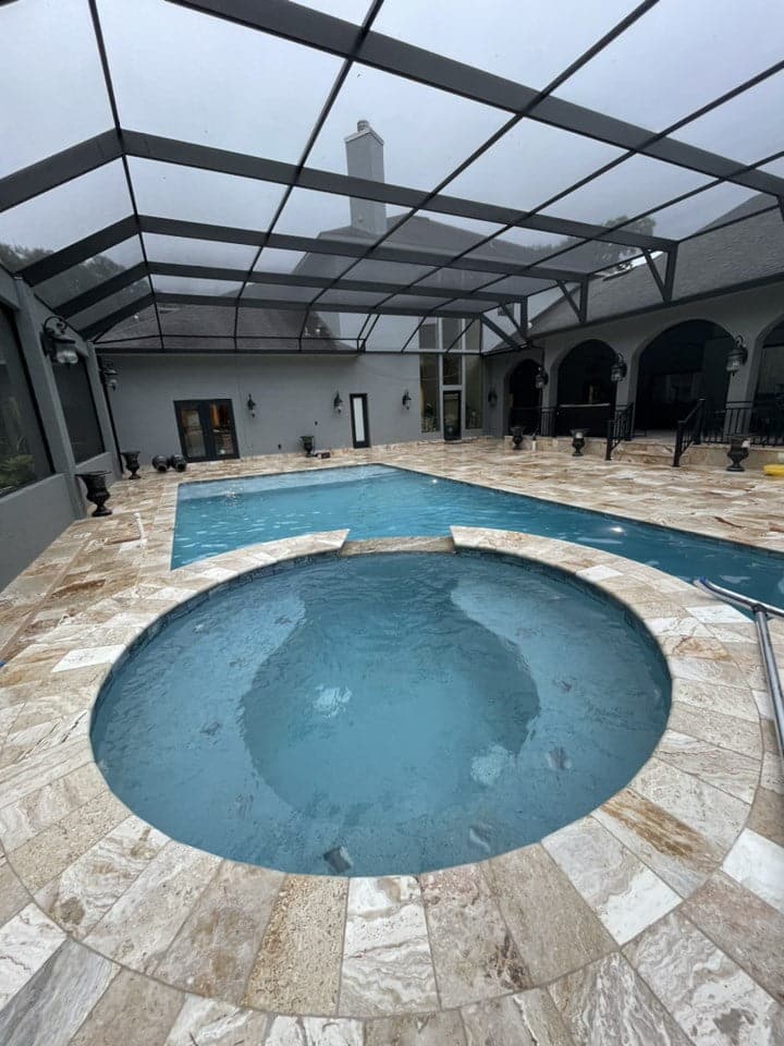 A large round spa dominates the foreground with a rectangular pool behind it under a screened enclosure.