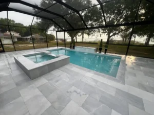A rectangular pool with a raised elevated spa and tiled deck under a screen enclosure overlooking a lake.