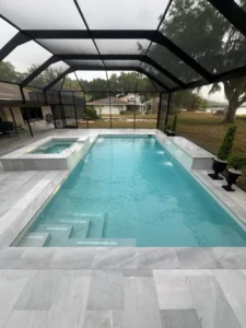 A rectangular pool with a raised spa and two water spouts under a screened lanai overlooking a lake.