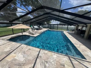 A rectangular pool with an attached spa under a screened enclosure with travertine deck.
