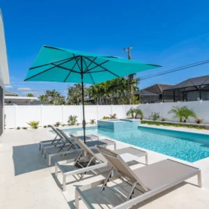 A small rectangular pool with a raised spa and lounge chairs under a teal umbrella in a fenced backyard.