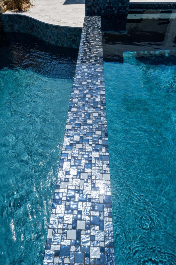 A close-up of a glittering mosaic tile wall dividing two sections of a pool.