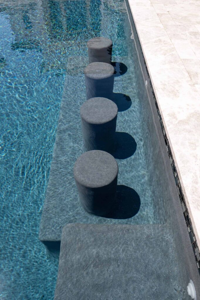 Close-up of round stone stools set into a shallow pool ledge beside travertine decking.
