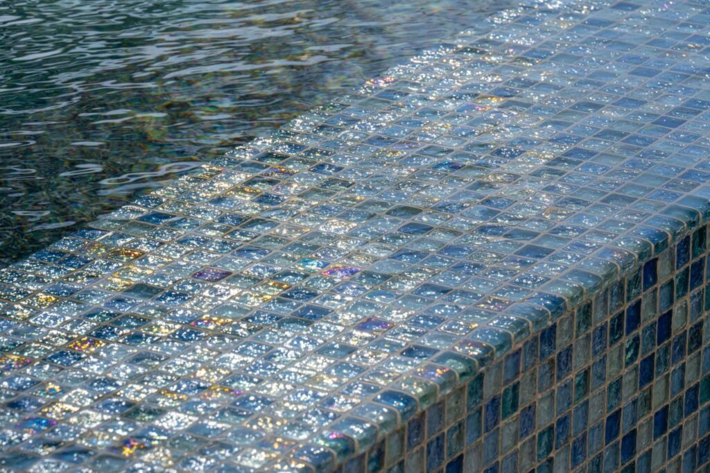 Close-up of sparkling glass mosaic tile edge on a pool step with water lapping beside it.