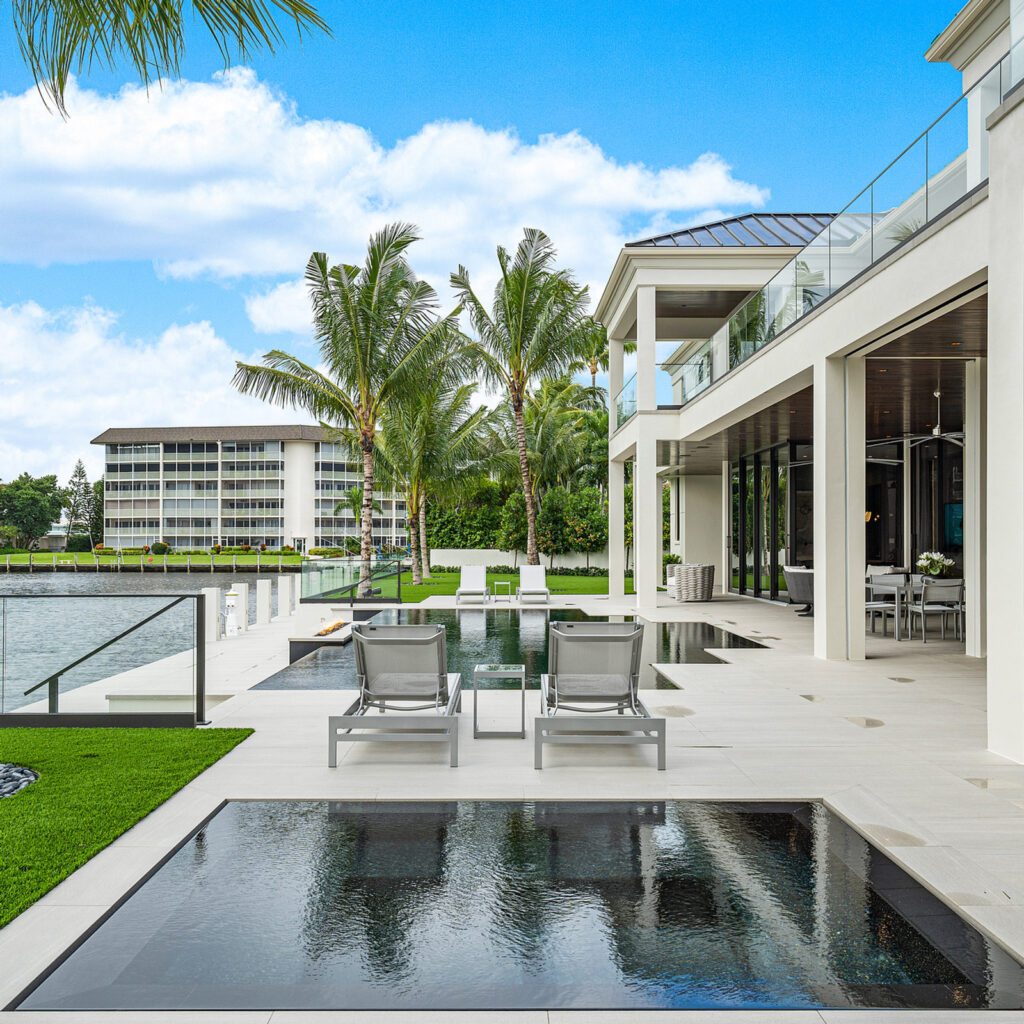 A sleek dark reflecting pool leads toward additional pool sections on a waterfront modern estate deck.