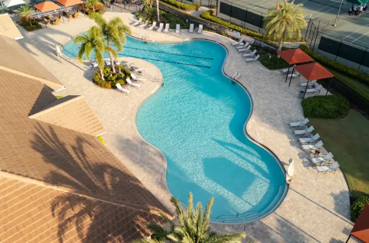 Aerial view of a large freeform resort-style pool surrounded by palm trees, loungers, and tennis courts.