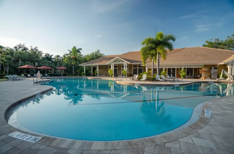 A large freeform community pool in front of a clubhouse with palm trees and lounge chairs.
