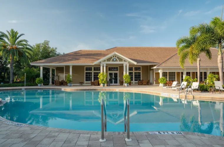 A large freeform community pool in front of a clubhouse with palm trees and lounge chairs.