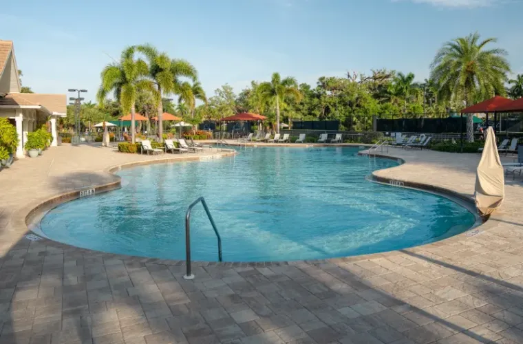 A large freeform community pool surrounded by paver decking, loungers, and palm trees under open sky.