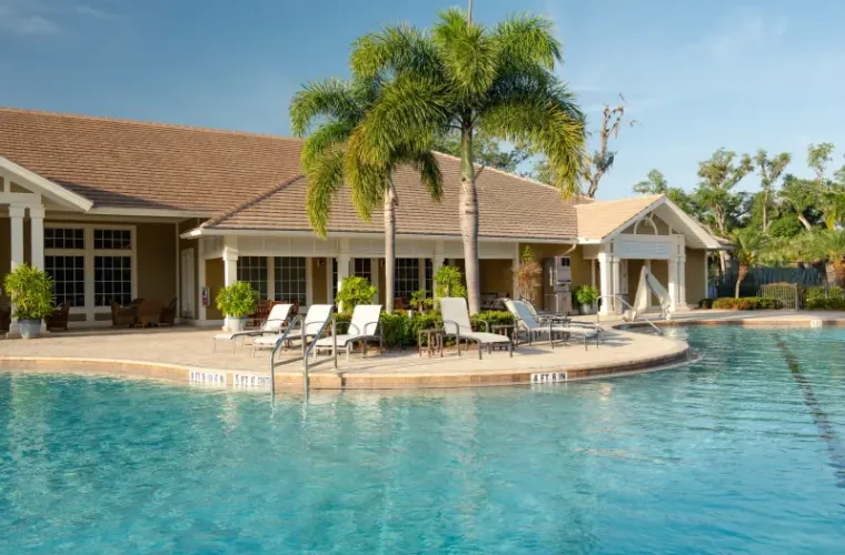A resort-style pool with lounge chairs and palm trees in front of a clubhouse building.
